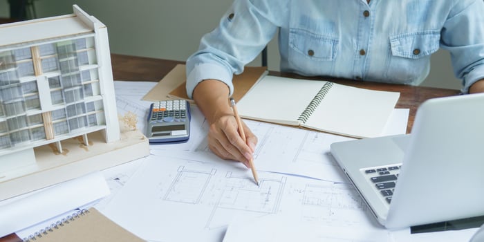 Construction estimator working with blueprints, calculator, and project documents to build an accurate project estimate